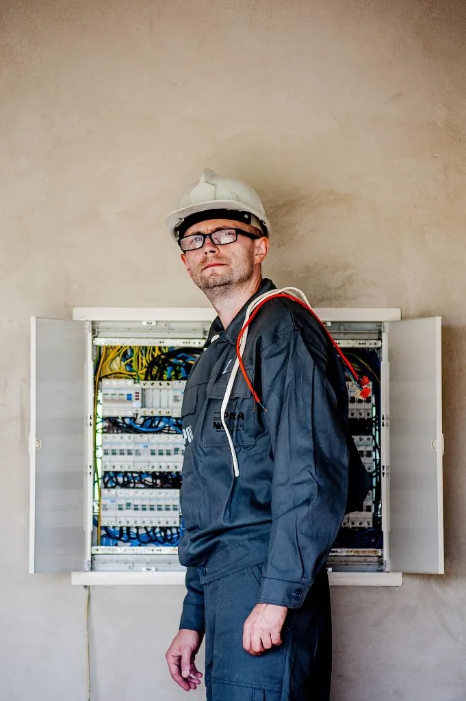 Electrician in a hard hat standing beside an open electrical panel